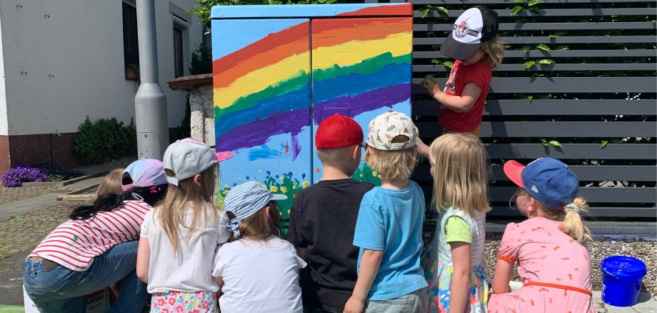 Kinder bemalen einen Stromkasten mit einem Regenbogen